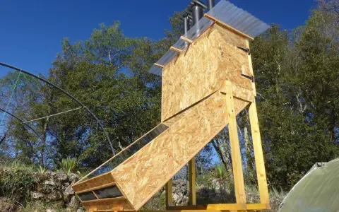 Un sechoir solaire artisanal en bois, avec un panneau incliné vitré, sous un ciel bleu.