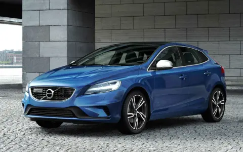 Niebieskie Volvo V40 D2 z czarnym dachem, zaparkowane na kamiennej nawierzchni, z nowoczesną architekturą w tle.