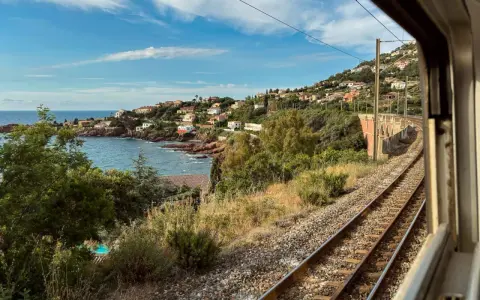 Blick aus dem Fenster eines Nachtzugs Paris Nizza auf eine Küstenlandschaft mit Häusern, Meer und Bahngleisen.