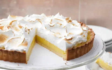 Eine köstliche Tarte au Citron mit fluffiger Baiserhaube, die auf einem Tortenständer präsentiert wird.