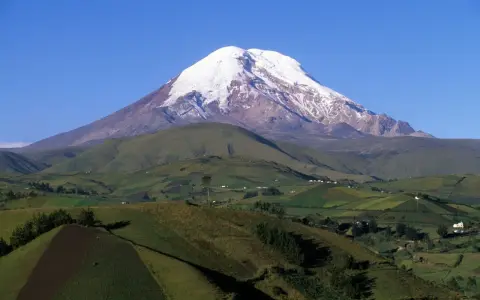 Ośnieżony wulkan Chimborazo, najwyższy szczyt Ekwadoru, góruje nad zielonymi wzgórzami, przypominając majestatem nawet Everest.