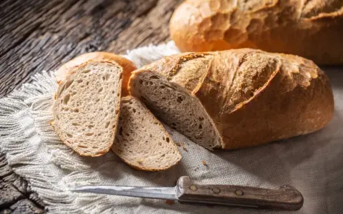 Chleb z kaszy jaglanej, pokrojony na kromki, leży na lnianej serwetce obok noża.