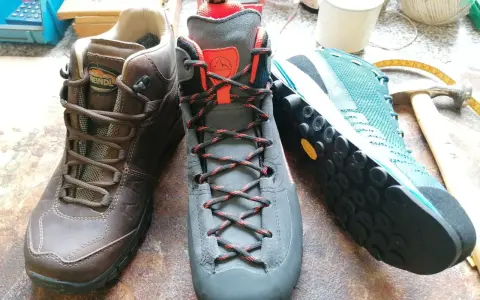 Drei Wanderschuhe von verschiedenen Herstellern: braun, grau und türkis. Werkzeuge und Garn liegen daneben.