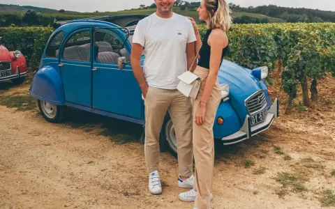 Couple souriant devant une 2CV bleue dans les vignes, une belle idée pour visiter Beaune en 1 jour.