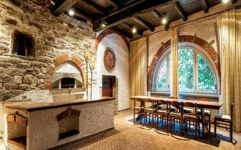 Tavernetta moderna piccola con forno a legna in pietra, bancone in muratura e un lungo tavolo in legno con sedie.
