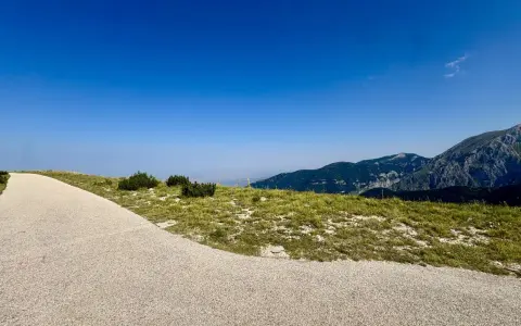 Sentiero ghiaioso verso la cima Blockhaus, con prati verdi e montagne sullo sfondo sotto un cielo azzurro.