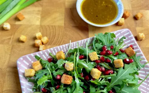 Frischer Rucola Salat mit Granatapfelkernen und Croutons, dazu ein Dressing.