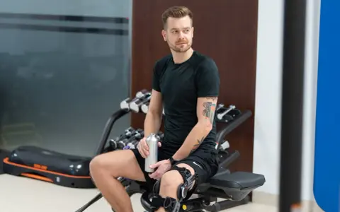 Mężczyzna w ortezie na kolanie odpoczywa po treningu. Jego rehabilitacja po operacji łąkotki przebiega pomyślnie.