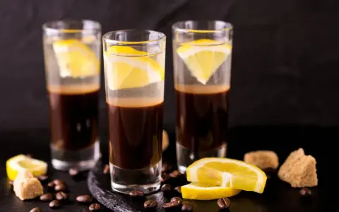 Drei Gläser mit Espresso und Zitrone, ein italienischer Genuss. Kaffeebohnen und Zuckerwürfel liegen daneben.