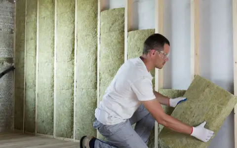 Un ouvrier installe des panneaux d'isolant dans un mur en bois. Il est important de connaître le prix au m2 pour l'isolation intérieure afin de maîtriser son budget travaux.