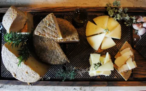 Tabla de quesos variados, hierbas aromáticas y ajos sobre madera.