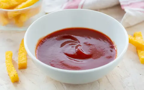 Una ciotola di ketchup fatto in casa, pronto per intingere bastoncini di polenta dorati.