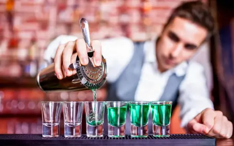 Barman nalewa zielony alkohol do kieliszków.
