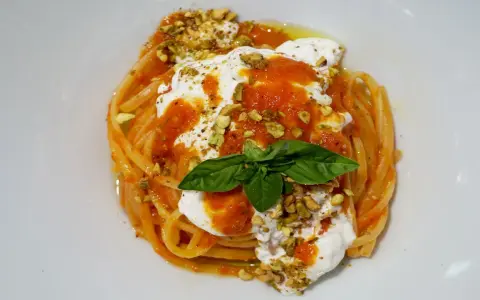 Un piatto invitante di pasta con stracciatella, salsa di pomodoro, pistacchi tritati e una foglia di basilico fresco.