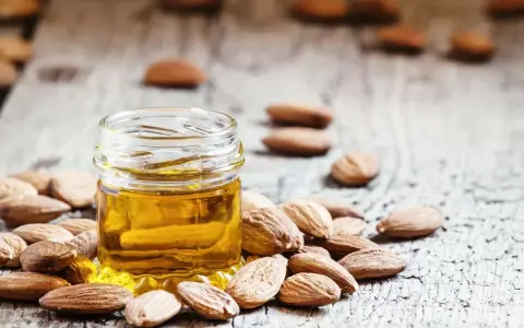 Aceite de almendras para que sirve: un frasco de aceite dorado rodeado de almendras sobre madera rústica.