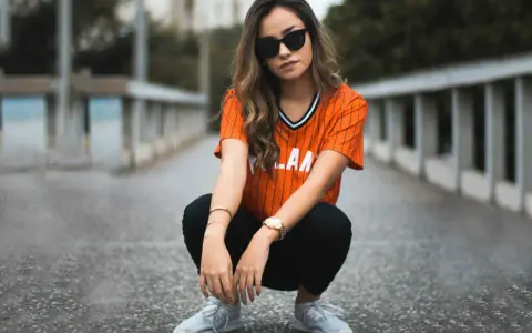 Mujer con estilo smart casual, con camiseta naranja a rayas, pantalones negros y zapatillas deportivas.