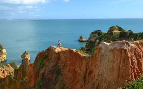 Zwei Wanderer genießen die milden Temperaturen Portugals im November an einer Klippe mit Blick auf das Meer.