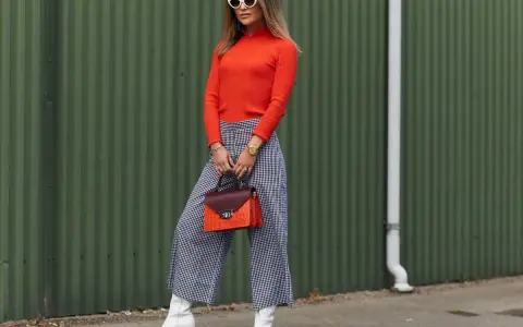 Modna kobieta w pomarańczowym golfie i kraciastych kulotach, białych kozaczkach i okularach. Stylowe kuloty stylizacje.