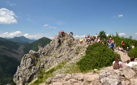 Grupa turystów odpoczywa na skalistym szczycie, podziwiając widok na **Dolinę Białego**.
