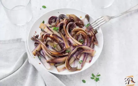 Radicchio in padella, caramellato e profumato, servito su un piatto bianco con un tocco di erbe aromatiche.