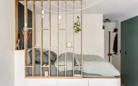 Aménagement astucieux d'un studio T2 avec un lit douillet séparé par une étagère en bois.