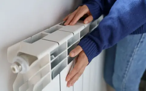 Manos frías tocan un radiador blanco que no calienta.
