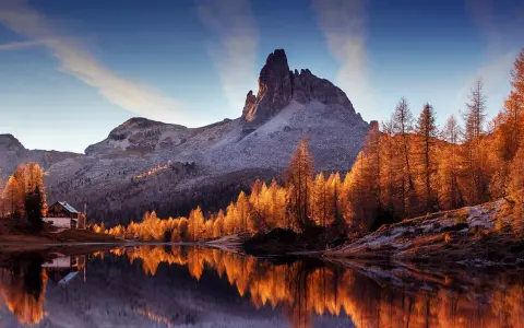 Riflessi dorati sull'acqua di un lago alpino, con un rifugio e montagne innevate. Perfetto per le camminate a Cortina d'Ampezzo.