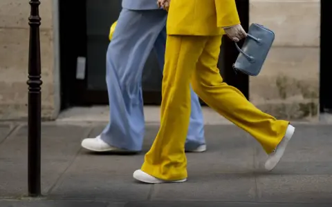 Un outfit tailleur con sneakers, giallo brillante e azzurro polvere, camminano sul marciapiede.