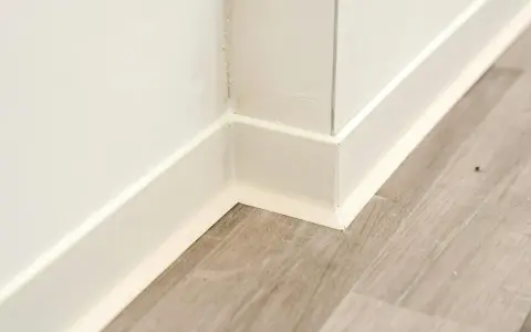 Angolo di una stanza con parquet grigio e battiscopa bianco appena installato.