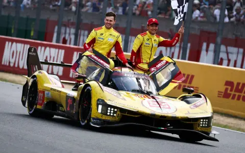 Zwei Rennfahrer in gelb-roten Overalls jubeln neben ihrem gelben Ferrari Le Mans Prototyp mit der Startnummer 83.