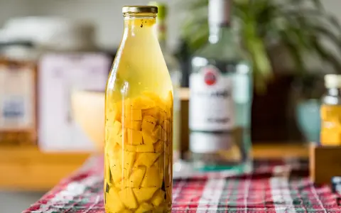 Bouteille de rhum arrangé mangue, avec des morceaux de fruits jaunes et des épices.