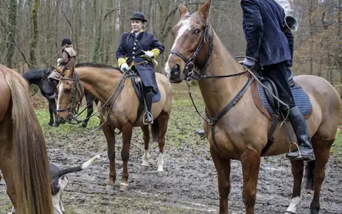 Cavaliers en tenue de chasse à courre, prêts pour l'aventure dans la forêt boueuse.