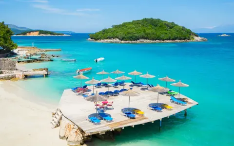 Rajskie widoki na **Albania najpiękniejsze plaże**. Turkusowa woda, piaszczysta plaża i drewniany pomost z leżakami.