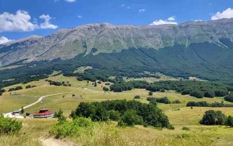 Vasta distesa verde ai piedi del monte Mileto, con un edificio circolare rosso e una strada tortuosa.