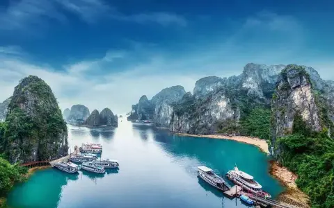 Widok na Zatokę Ha Long, kiedy do Wietnamu. Statki cumują przy turkusowej wodzie, otoczone wapiennymi wyspami porośniętymi zielenią.