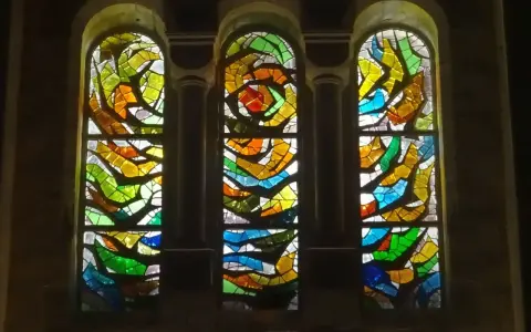 Trois vitraux aux formes abstraites et aux couleurs vives, un exemple de comment éclairer un vitrail pour révéler sa beauté.
