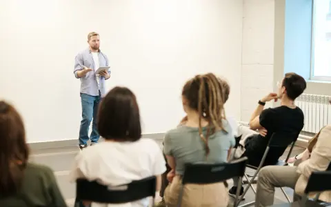 Mężczyzna z tabletem przemawia do grupy słuchaczy. Widać, że jego **charyzma co to** jest widoczna w sposobie, w jaki angażuje publiczność.