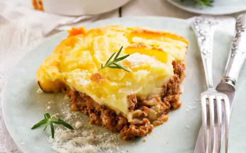 Zapiekanka pasterska (Shepherd's Pie) z warstwą mielonego mięsa i ziemniaków, ozdobiona rozmarynem.