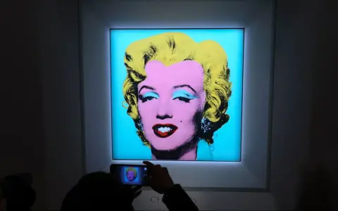 A person photographs Andy Warhol's iconic Marilyn Monroe printmaking, capturing the vibrant colors and pop art style.