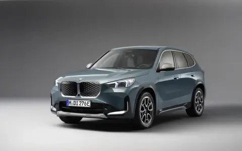 BMW iX1 w kolorze zielonym, widok z przodu, na szarym tle.