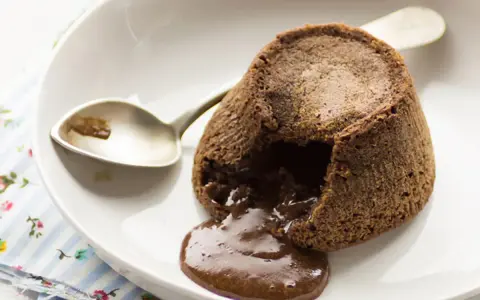 Coulant de chocolate recién hecho, con su interior líquido y cremoso desbordándose. Una cuchara plateada espera pacientemente.