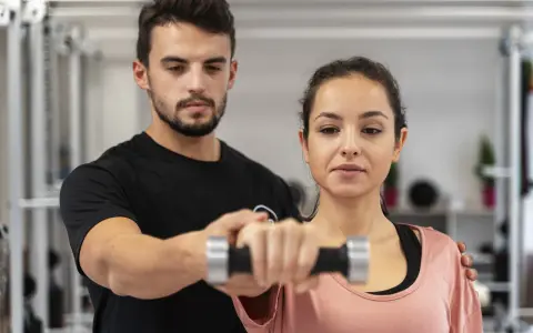 Fizjoterapeuta pomaga kobiecie w ćwiczeniach z hantlem, wspierając jej regenerację po treningu.