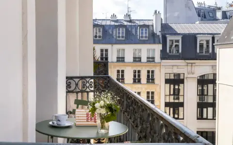 Petit-déjeuner sur le balcon avec vue sur les toits de Paris. Une tasse de café, un livre "Paris mon amour" et des fleurs, un moment de détente au saint-grégoire.