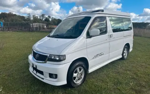 Biały van Mazda Bongo z podnoszonym dachem, zaparkowany na trawie.