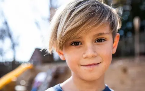 Ein Junge mit blonden Haaren, die nach vorne fallen, lächelt in die Kamera.