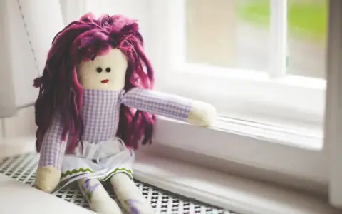 Bambola con capelli viola, vestita a quadretti, seduta sul davanzale. Un simbolo di conforto nella doll therapy per l'Alzheimer.