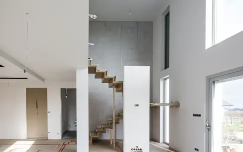 Nowe schody dywanowe w nowoczesnym domu w trakcie budowy. Drewniane stopnie kontrastują z betonową ścianą.