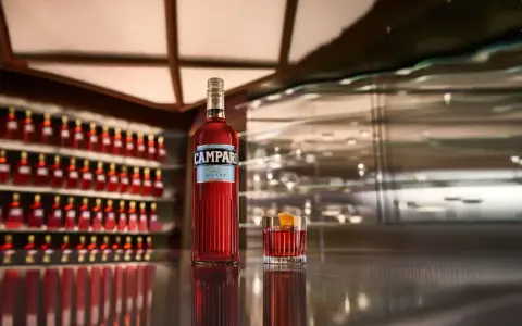 Eine Flasche Campari und ein Glas mit dem roten Aperitif stehen auf einer glänzenden Theke. Die Frage "wie schmeckt Campari?" wird durch den Anblick des ikonischen Getränks aufgeworfen.