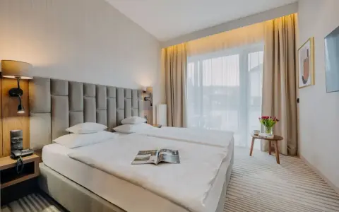 Przytulny executive room z dwoma wygodnymi łóżkami, lampkami nocnymi i dużym oknem z zasłonami. Na stoliku bukiet tulipanów.