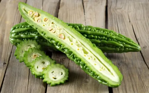 A halved bitter melon plant reveals its seedy interior, with sliced rounds fanned out on a rustic wooden surface.